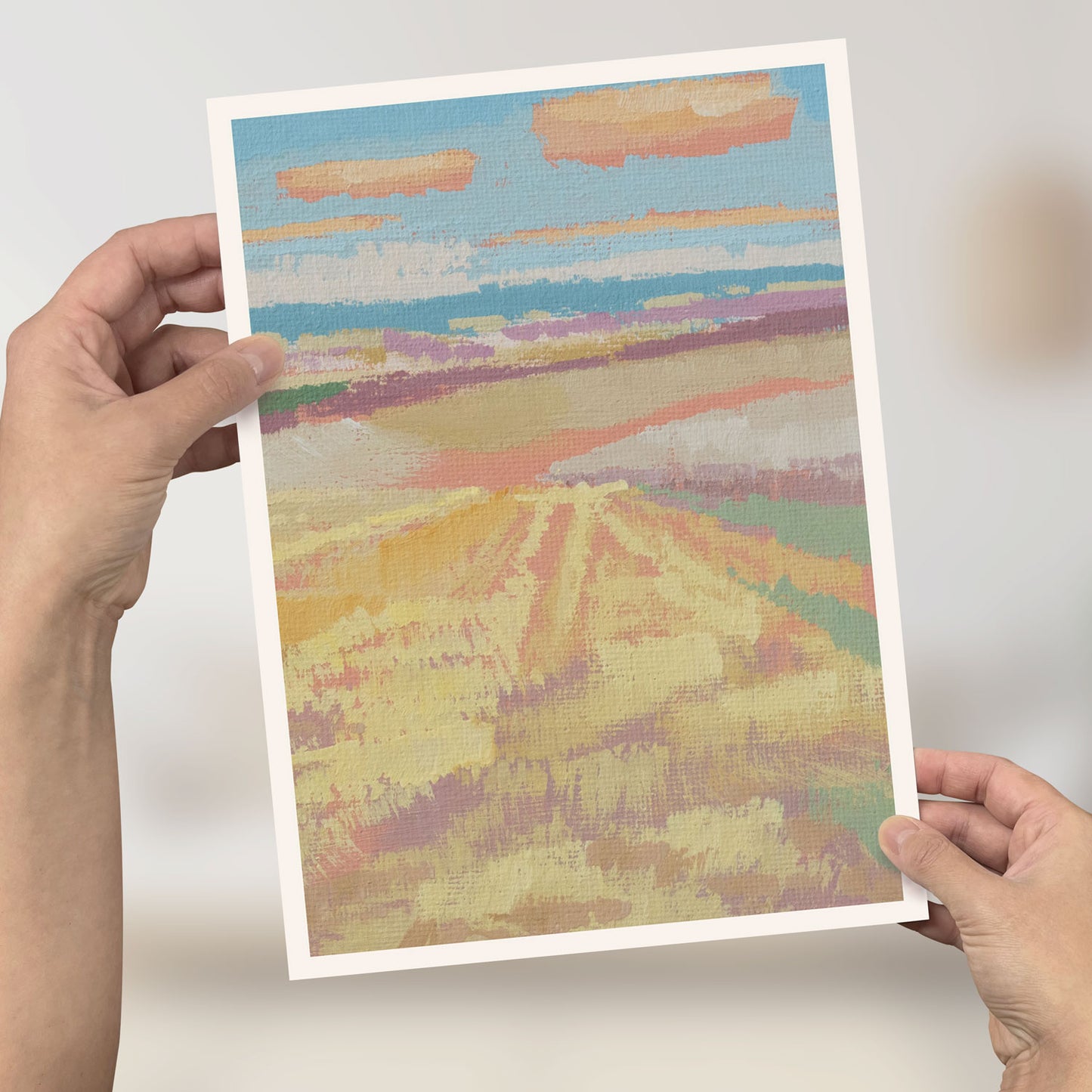 Person hält ein Mini-Poster mit malerischem Landschaftsmotiv in Himmelblau und Wolken, DIN A4.