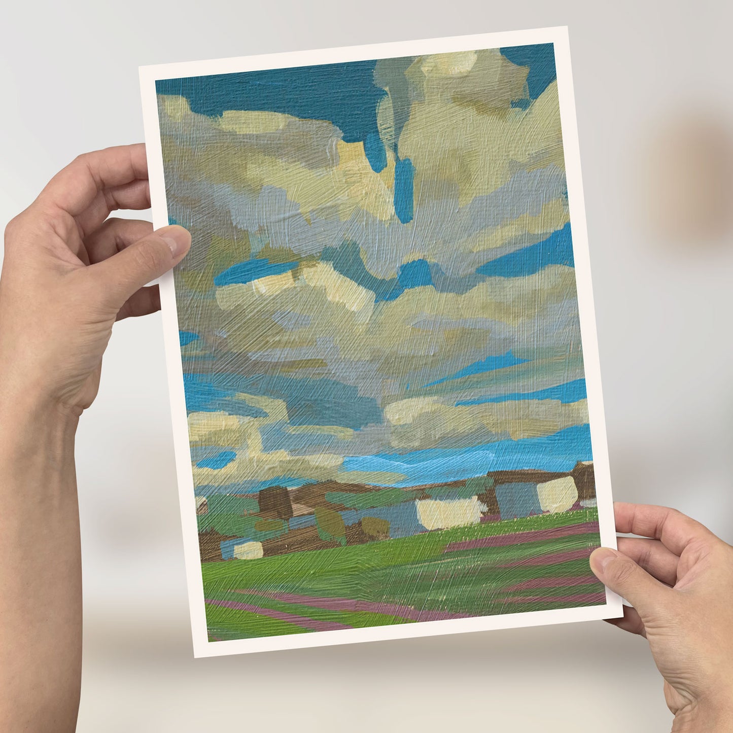 Jemand hält ein Mini-Poster mit malerischem Wolkenhimmel im Format 21x29,7 cm, hochwertiges Recyclingpapier.